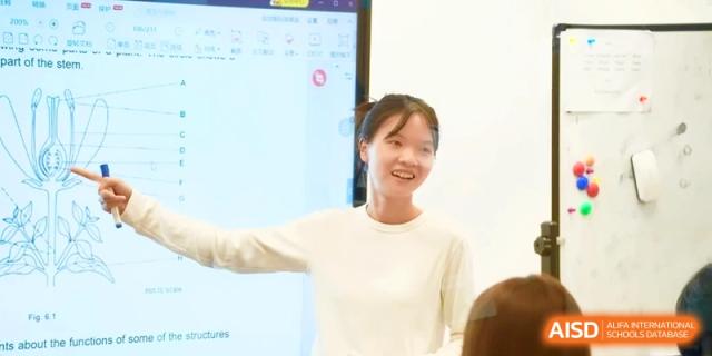A female teacher smiling while presenting a lesson to her students in a bright, modern classroom at HT Nanjing Impact Academy.