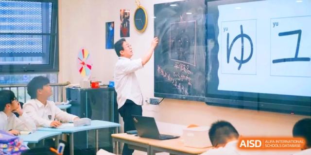 A teacher pointing at a large chalkboard while conducting a lesson for students in a well-equipped, modern classroom at HT Nanjing Impact Academy.