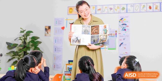 A smiling female teacher showing an illustrated book to her engaged primary school students during class at HT Nanjing Impact Academy.
