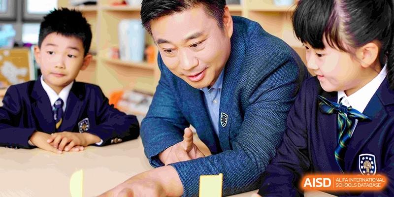 A male staff member or teacher smiling warmly while interacting with students during a school activity at HT Nanjing Impact Academy.