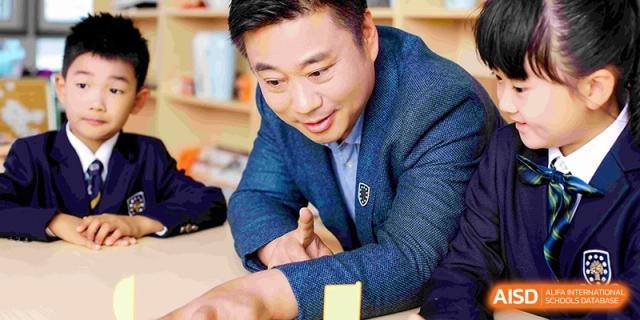 A male staff member or teacher smiling warmly while interacting with students during a school activity at HT Nanjing Impact Academy.