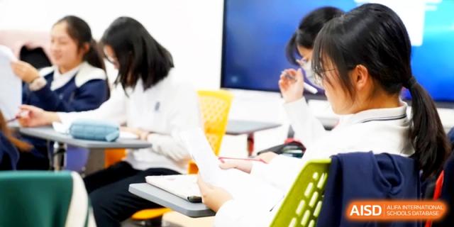 Students sitting at their desks and taking notes during a focused academic lesson in a modern classroom at HT Nanjing Impact Academy.