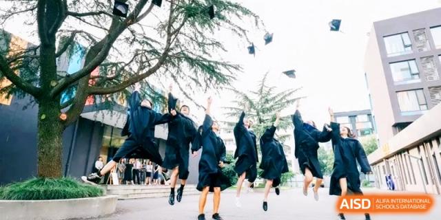 Graduates in black gowns jumping for joy and throwing their caps in the air to celebrate their success at HT Nanjing Impact Academy.