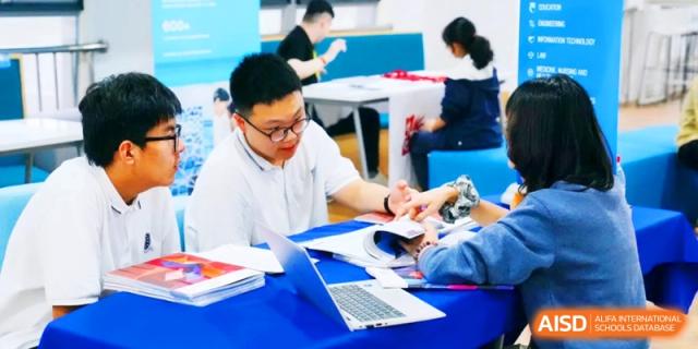 A teacher and students sitting at a round table discussing course materials and using a laptop for study at HT Nanjing Impact Academy.