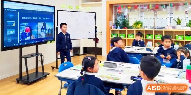 Young students engaged in a classroom discussion while sitting at shared tables in a brightly lit room at HT Nanjing Impact Academy.