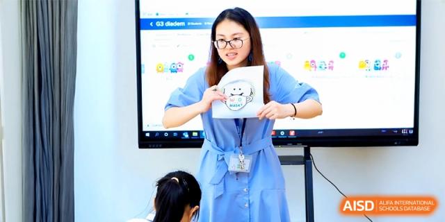 A teacher holding up a visual aid while standing in front of an interactive digital screen during a class at HT Nanjing Impact Academy.
