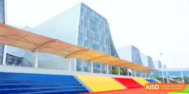 Modern campus architecture featuring a large glass building and colorful red and yellow stadium seating at HT Nanjing Impact Academy.