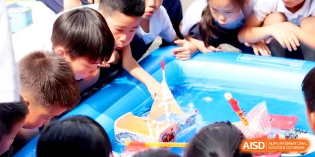 Children gathered around an inflatable pool, launching and playing with colorful handmade paper boats at HT Nanjing Impact Academy.