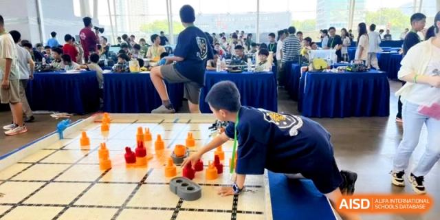 A student focused on a tabletop strategy game or robotics challenge during an indoor competition at HT Nanjing Impact Academy.