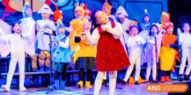 Students in vibrant costumes performing a dance routine on a stage with professional blue lighting at HT Nanjing Impact Academy.