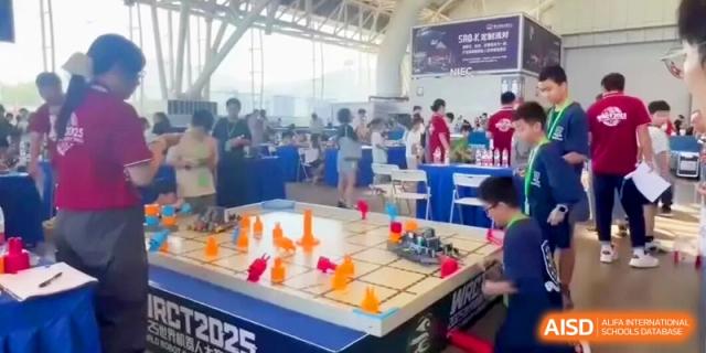 An indoor robotics arena where students are testing and competing with small robots on a labeled game board at HT Nanjing Impact Academy.