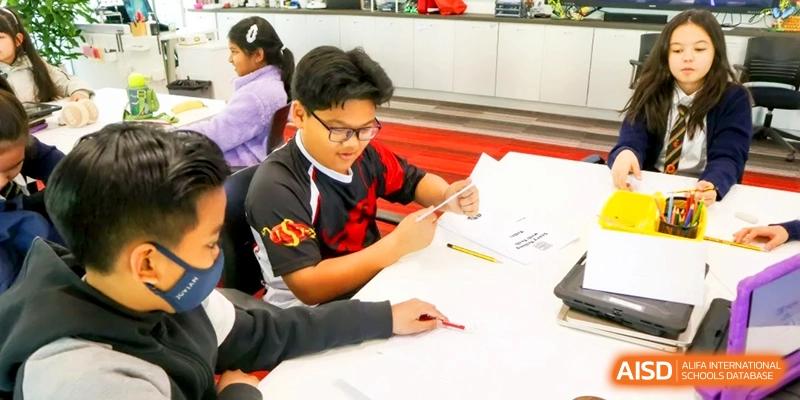A student wearing a school jersey looks closely at a paper while working on a hands-on activity at a desk in a classroom at the International School of Tianjin.