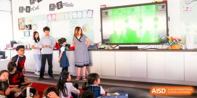 A student stands at the front of a classroom giving a presentation to her seated peers at the International School of Tianjin.