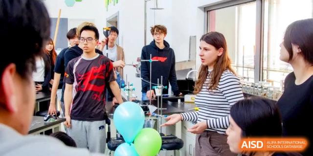 A group of students discusses a science project near lab equipment and colorful balloons at the International School of Tianjin.