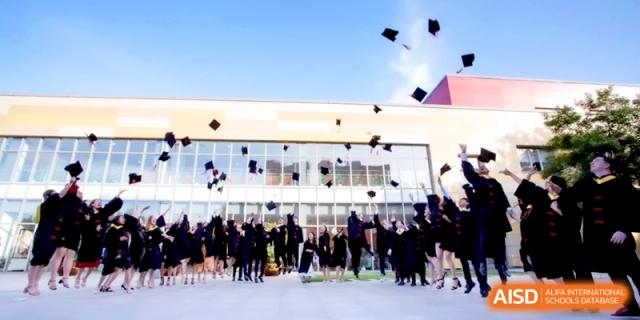 Graduates in black gowns throw their caps into the air in front of the campus building at the International School of Tianjin.