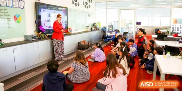 A teacher leads a lesson for students sitting on a red rug in a modern primary classroom at the International School of Tianjin.
