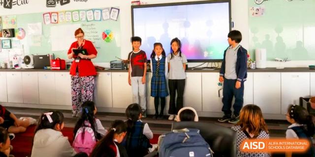 Three students stand in front of a digital screen presenting to their classmates at the International School of Tianjin.