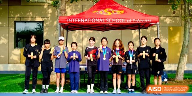 Students proudly display their medals and trophies under a red school tent at the International School of Tianjin.