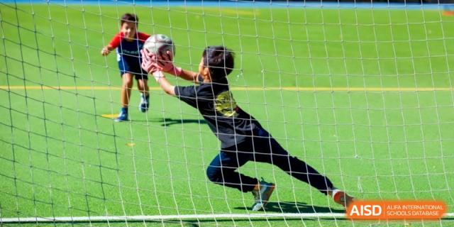 A young goalkeeper dives to make a save during a soccer match on the green field at the International School of Tianjin.