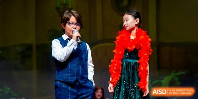 A young performer in a vest and tie sings into a microphone during a theater production at the International School of Tianjin.