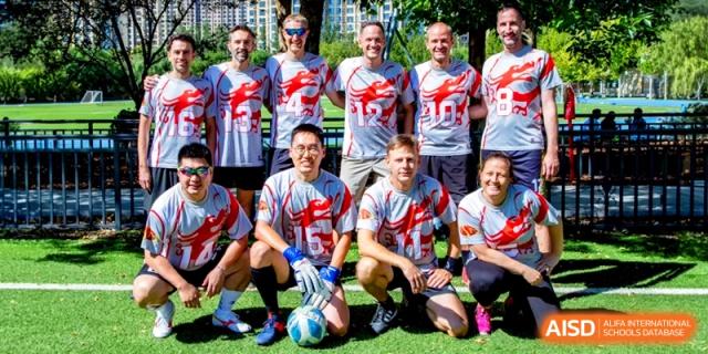 A team of adult coaches and staff pose together in matching athletic gear on the field at the International School of Tianjin.