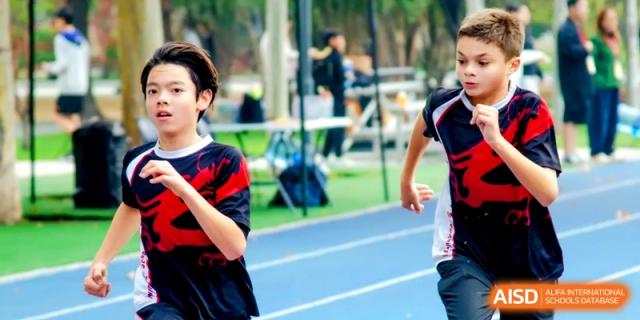 Two students in school uniforms race side-by-side during an outdoor track and field meet at the International School of Tianjin.