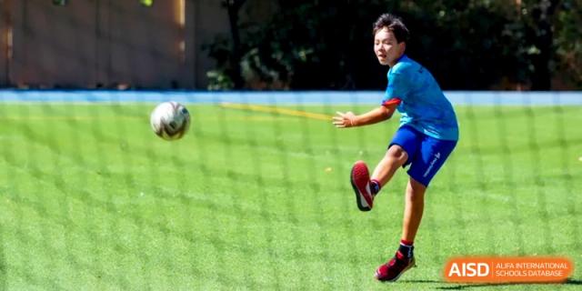 An action shot of a student kicking a soccer ball across the green turf during a game at the International School of Tianjin.