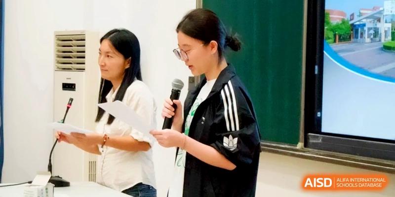 A female student in a black jacket speaks into a microphone while holding a script during an event at Xishan Senior High School.