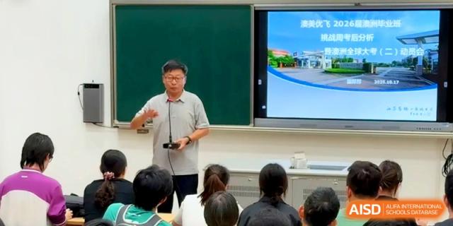 A male educator gestures during a presentation featuring a school campus image on a digital screen at Xishan Senior High School.