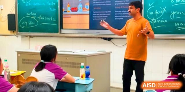 An instructor gestures toward a colorful digital presentation on a screen while teaching a class at Xishan Senior High School.