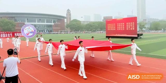 Students in white uniforms carry a large red banner across the sports field during a formal parade at Xishan Senior High School.
