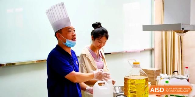 A professional chef in a white hat demonstrates baking techniques to a student in a well-equipped kitchen at Xishan Senior High School.