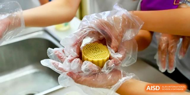 Hands in clear plastic gloves hold a perfectly molded, yellow mooncake during a cultural cooking activity at Xishan Senior High School.