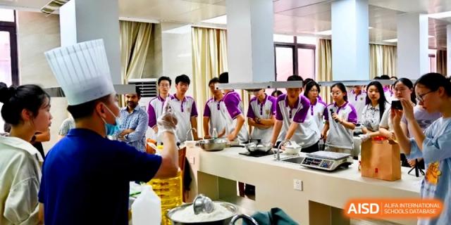 A class of students in purple uniforms works at long kitchen counters during a group culinary project at Xishan Senior High School.