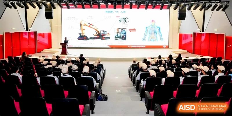 Students sit in a large auditorium watching a presentation about construction machinery on a large screen at Kunshan Senior High School.