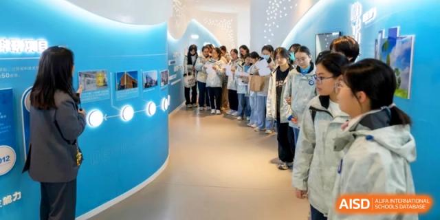 A group of students in white uniforms walk through a curved, modern exhibition hall with blue lighting at Kunshan Senior High School.