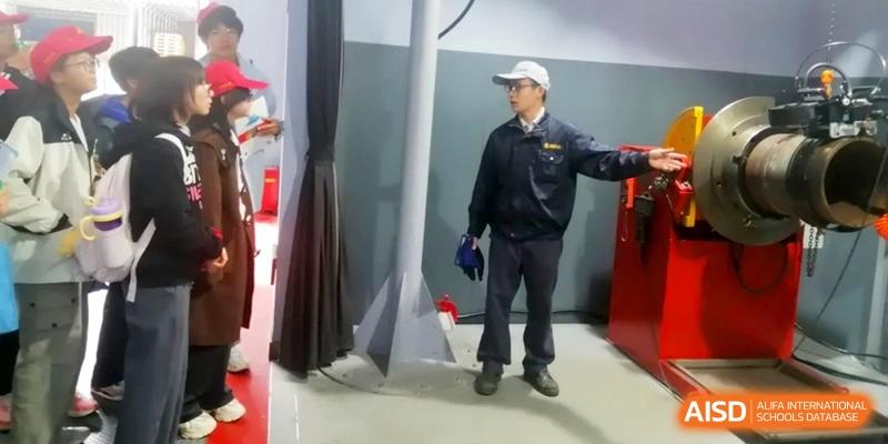 A man in a work uniform demonstrates technical equipment to a group of visiting students at Kunshan Senior High School.