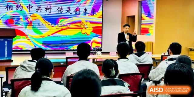 A speaker presents a colorful digital slide to a seated audience of students in a lecture hall at Kunshan Senior High School.