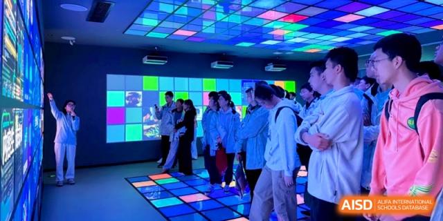 Students stand on a glowing, colorful interactive floor display in a high-tech showroom at Kunshan Senior High School.