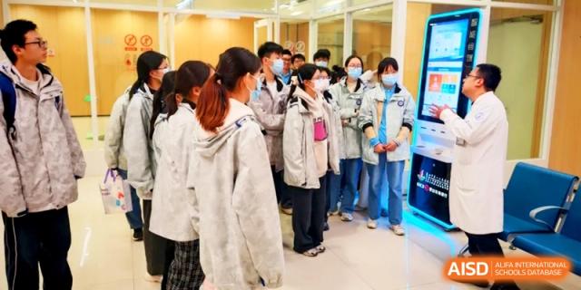 A group of students in matching white jackets gather in a modern hallway for a tour at Kunshan Senior High School.