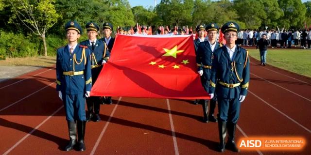 A student color guard carries a large national flag across the running track at Kunshan Senior High School.