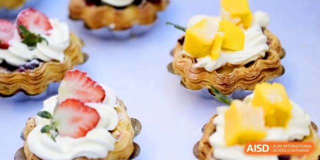 Fruit tarts topped with fresh strawberries, mango, and whipped cream are displayed on a white surface at Kunshan Senior High School.