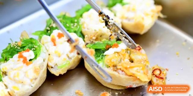 A close-up of tongs serving a savory stuffed pastry dish garnished with green herbs at Kunshan Senior High School.
