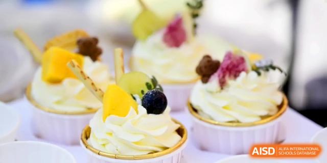 Several elegant cupcakes topped with yellow fruit, blueberries, and swirl frosting are ready for serving at Kunshan Senior High School.