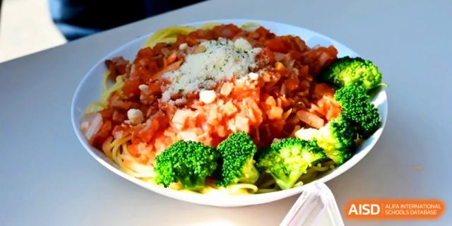 A plate of pasta topped with a rich tomato-based meat sauce and fresh broccoli florets at Kunshan Senior High School.