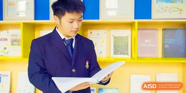 A student in a blue blazer focuses on reading a document while standing in a bright classroom at Maple Leaf International School - Xi_an.