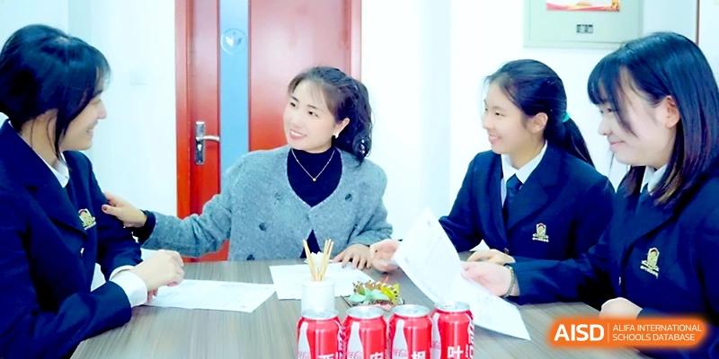 Two female students and a teacher share a smile while reviewing paperwork at a table at Maple Leaf International School - Xi_an.