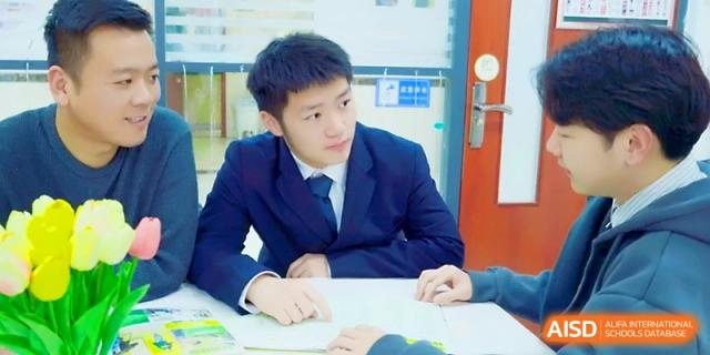 A male student in a formal school uniform sits at a desk and listens during a classroom discussion at Maple Leaf International School - Xi_an.