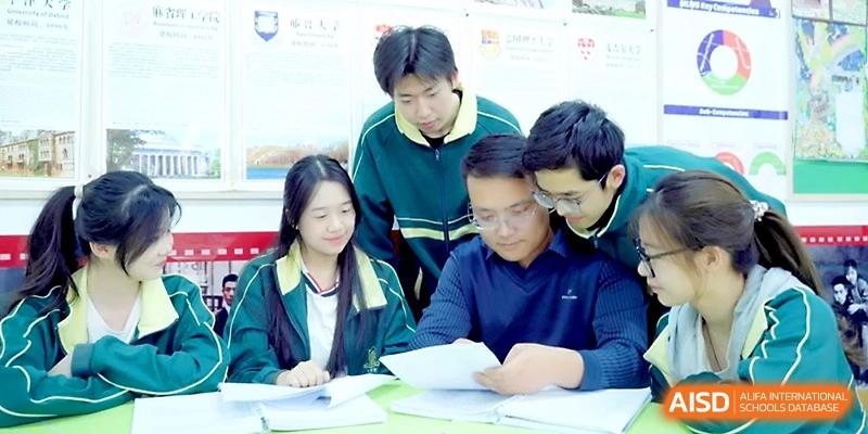 A group of students in matching tracksuits gathers around a desk to collaborate on a project at Maple Leaf International School - Xi_an.