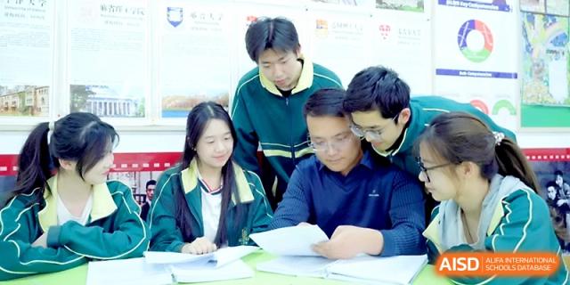 A group of students in matching tracksuits gathers around a desk to collaborate on a project at Maple Leaf International School - Xi_an.
